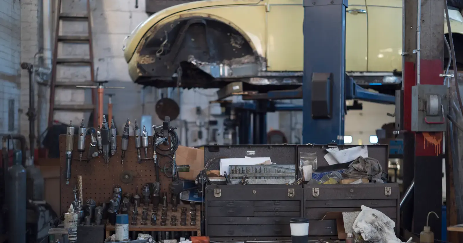 Il banco di un’officina meccanica, con gli attrezzi appesi al pannello, le cassette sul piano e sopra un’auto sul ponte sollevatore.