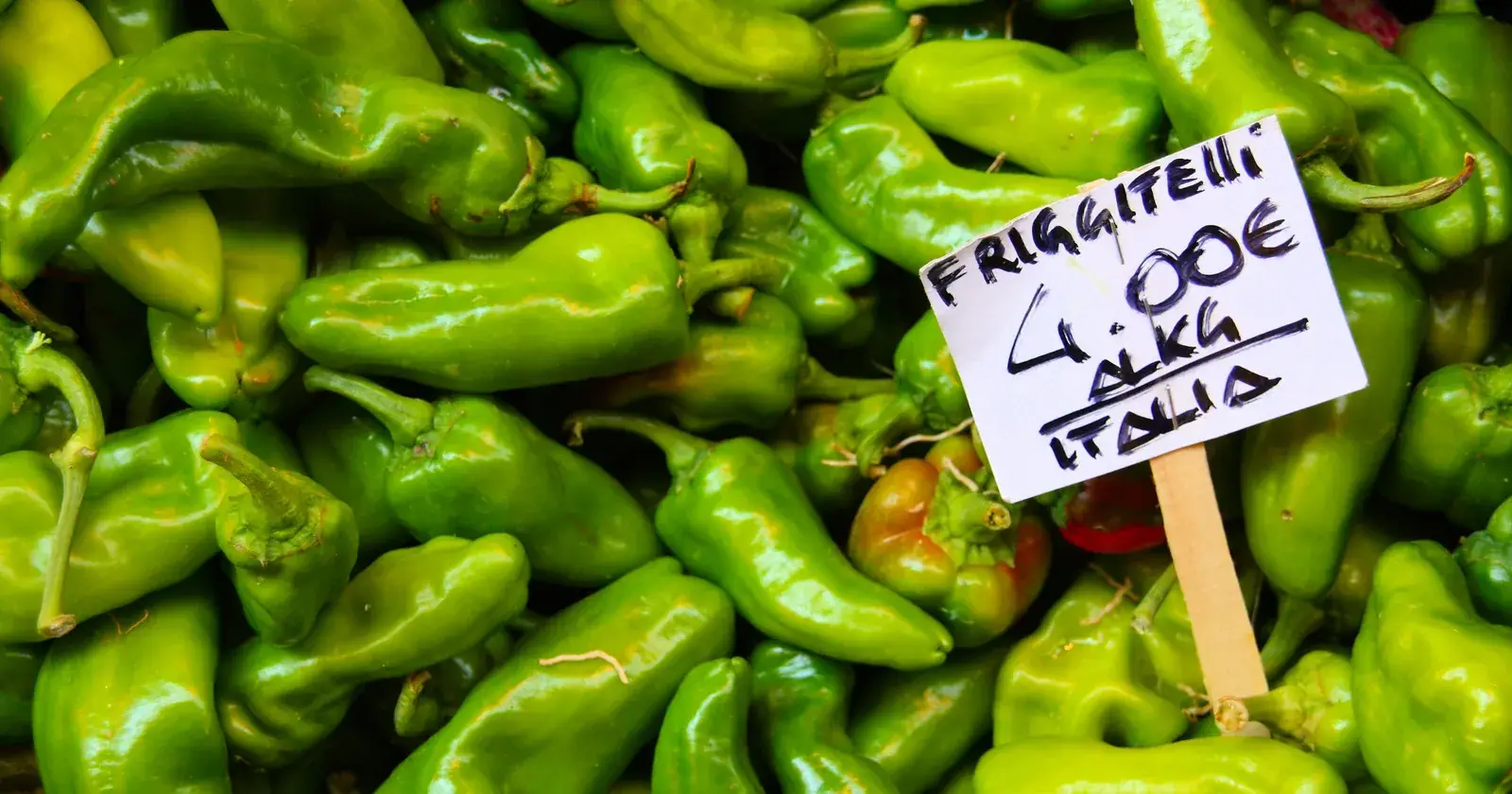 Friggitelli verdi al banco di un mercato di Bologna, con il cartellino del prezzo al chilo scritto a mano.